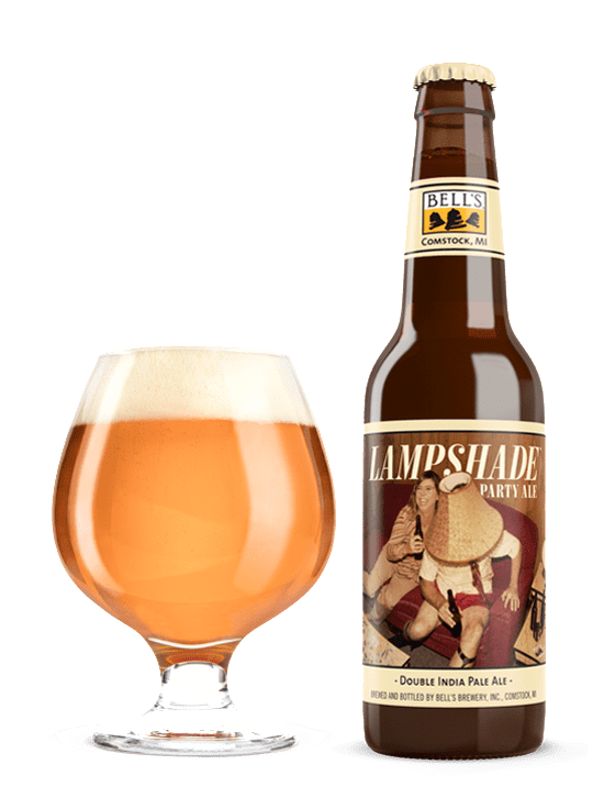 A full snifter glass sitting next to a bottle of Lampshade Party Ale