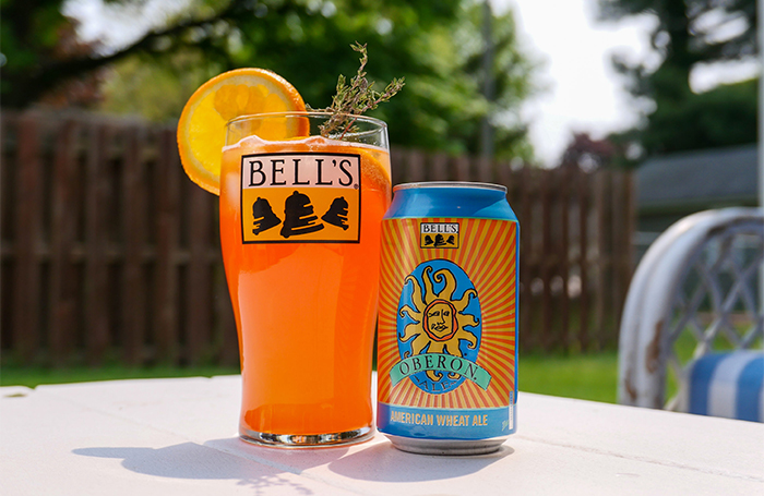 An Oberon Orange Aperol Beer Spritz: a can of Oberon next to an glass with orange liquid inside, with an orange on the top of it