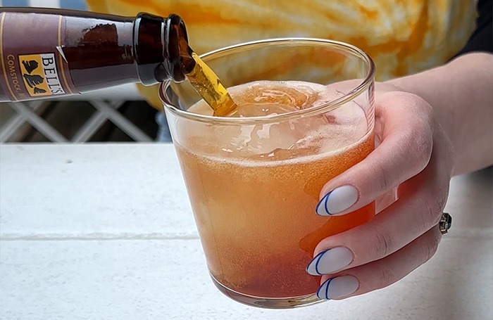 A bottle of Amber Ale being poured into a cocktail glass with a reddish liquid