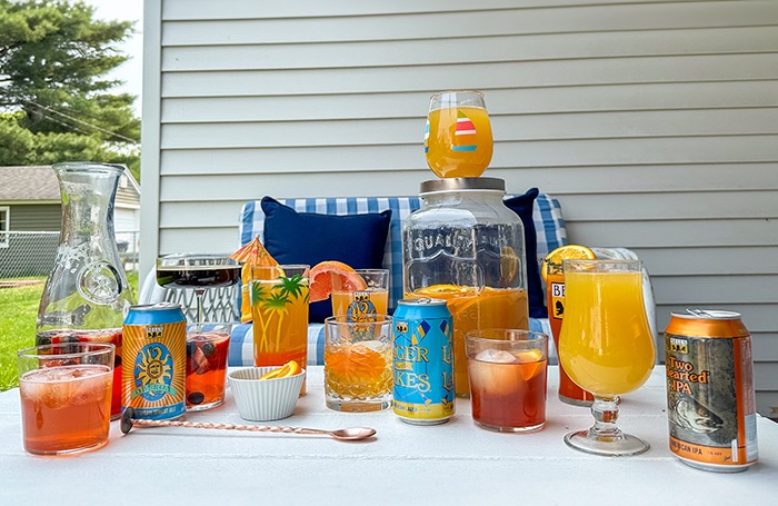 A table outside on a patio with several bottles and cans of Bell's beer with colorful cocktails near them