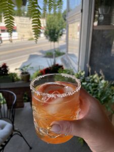 A hand holding a rocks glass with an orange liquid inside of it: A Two Hearted Paloma