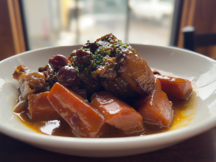 A meal of braised short rib with carrots and cherries served on a white plate with a blurred background.