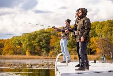 A group of men in camo outerwear fishing off of a dock on a lake